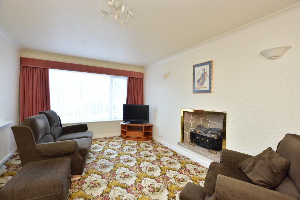 Living room with brown couches, floral carpet, fireplace, and a window with curtains.