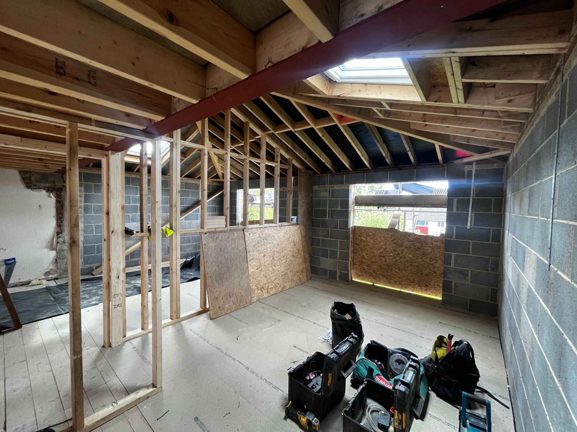 Interior construction in progress; framing, concrete block walls, red beam, tools, a skylight.