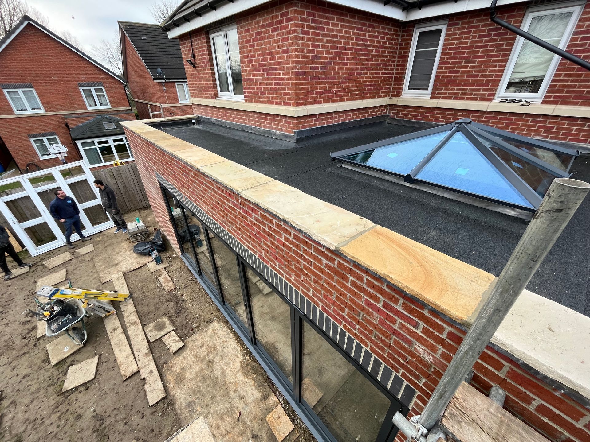 Construction site with red brick building extension, flat roof, skylight, and workers.