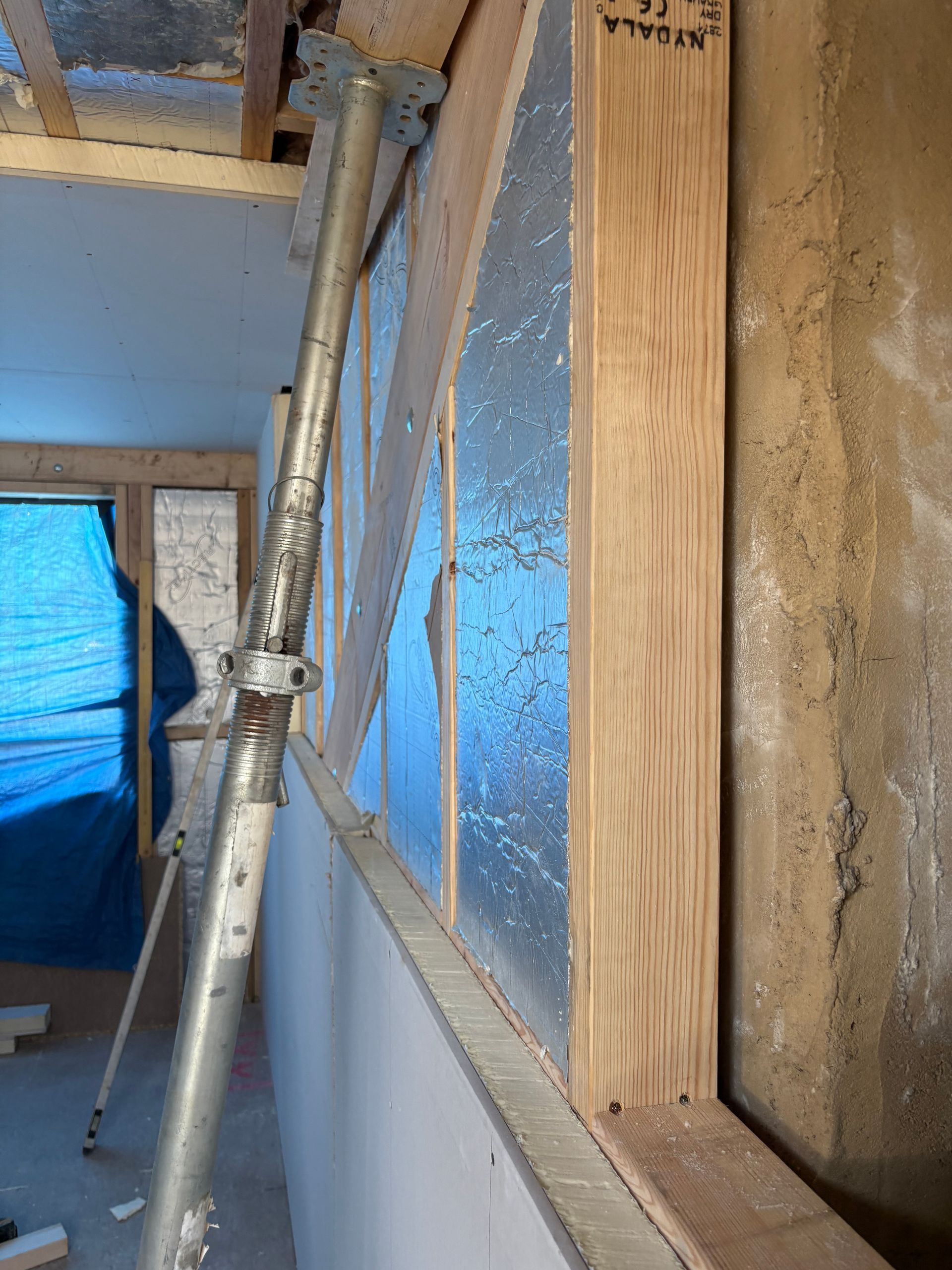 Interior view of a construction site with a wall framed in wood, insulation, and support beams.