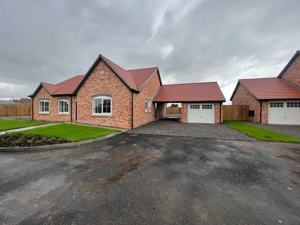 Brick bungalows with red tile roofs and garages under a cloudy sky.