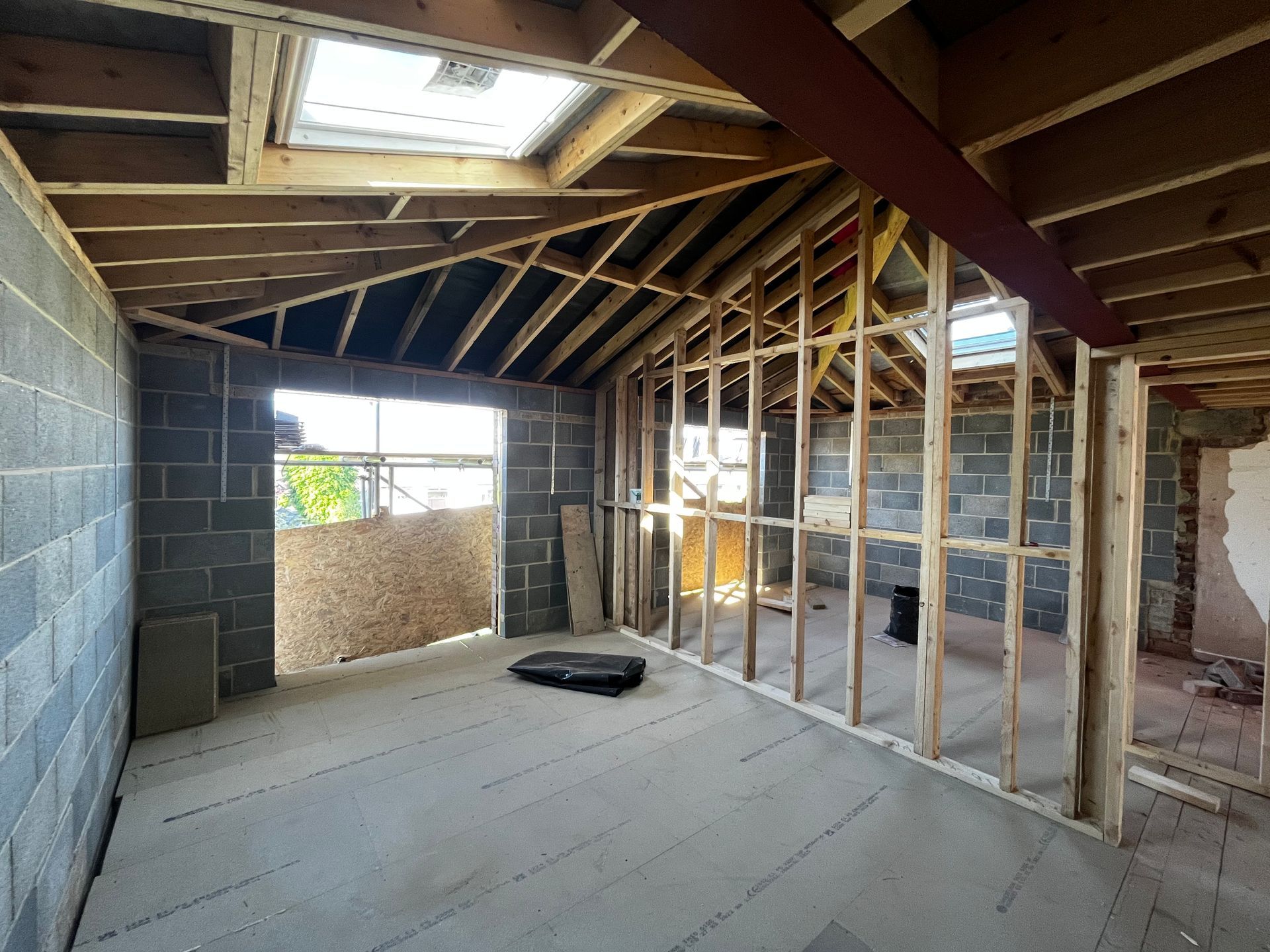 Interior of a room under construction with exposed beams, cinder block walls, and a window.