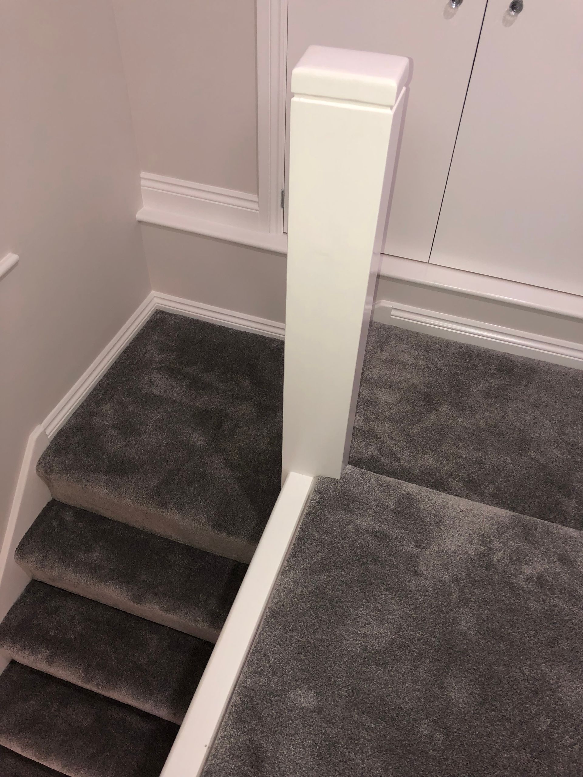 Staircase with gray carpet and white railing. A white post is on the landing.