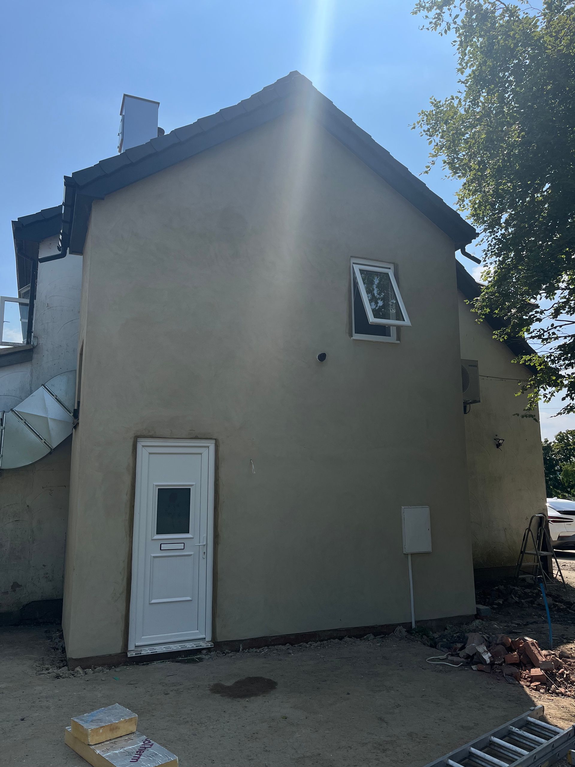 Side view of a light-colored building with a white door, window, and electrical box under a blue sky.