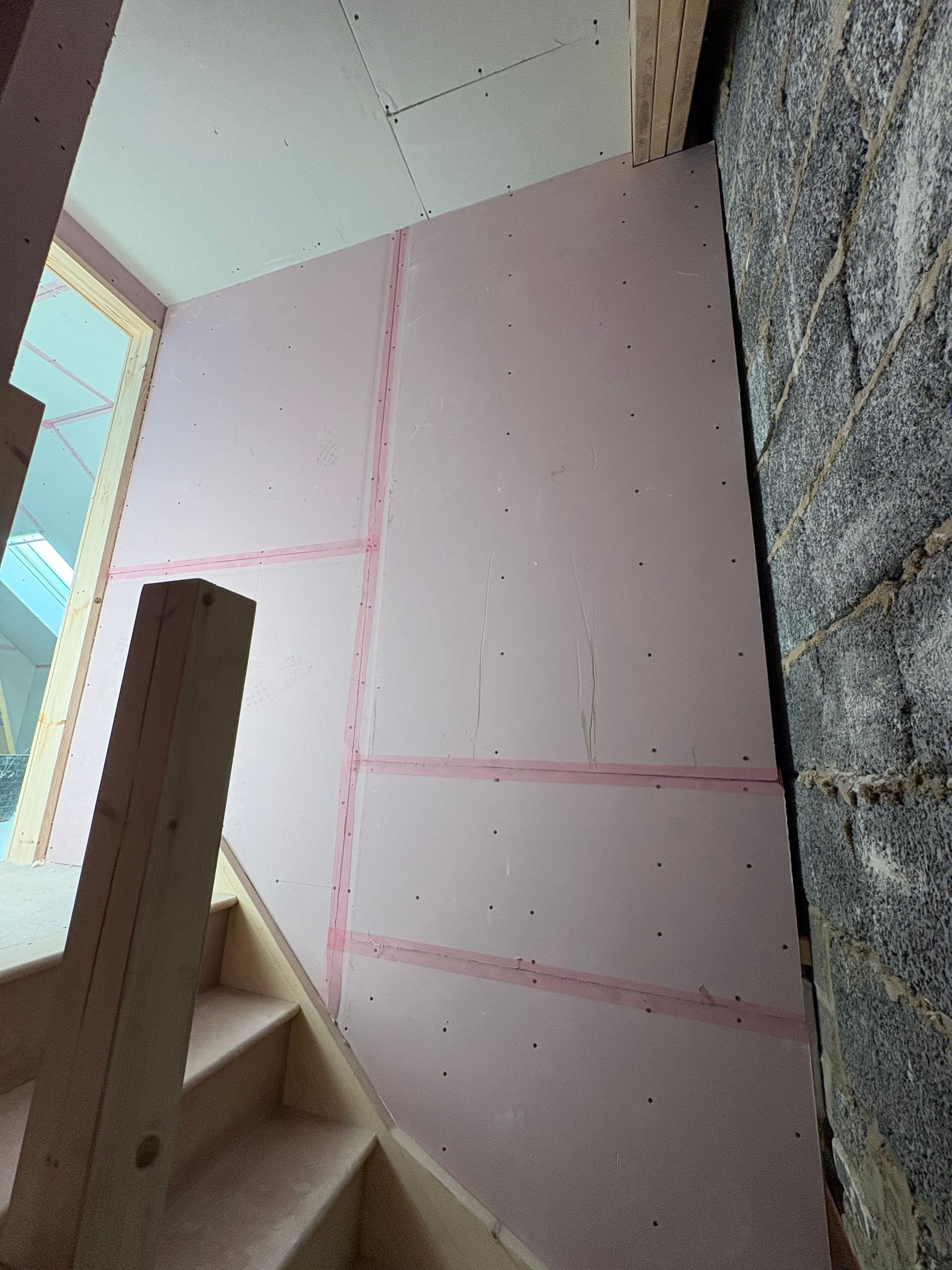 Pink insulated wall next to a staircase and brick wall.