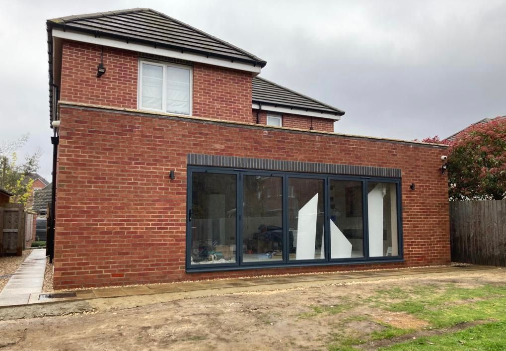 Red brick house with gray framed glass doors, overcast sky.