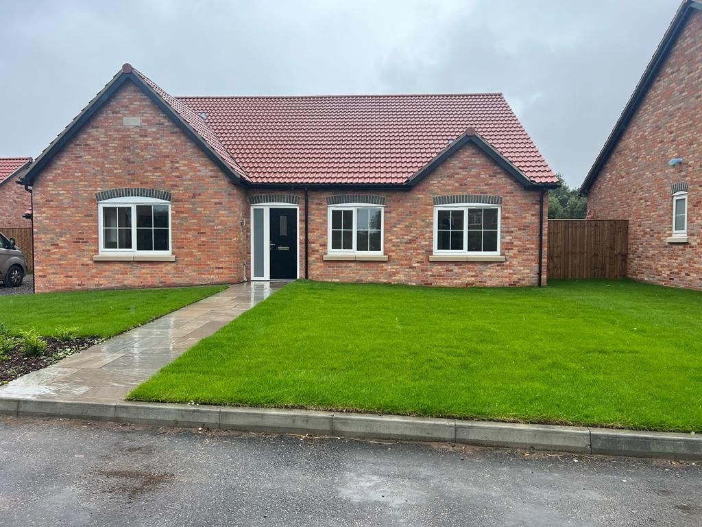 Red brick bungalow with green lawn and a gray sidewalk.