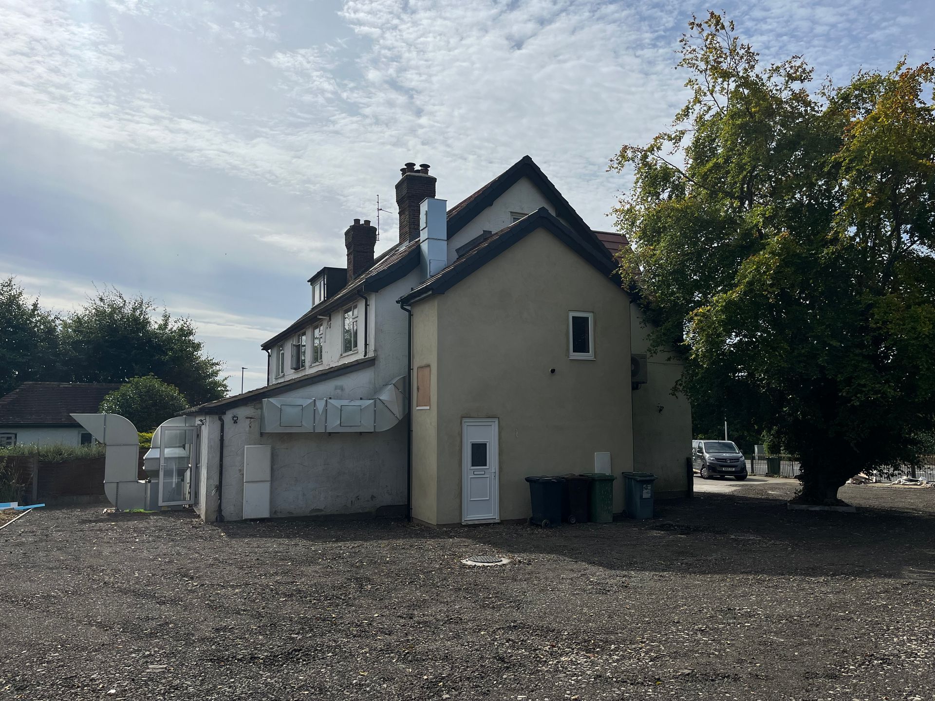 Side view of a two-story building with a tree on the right. A car is parked in the distance.