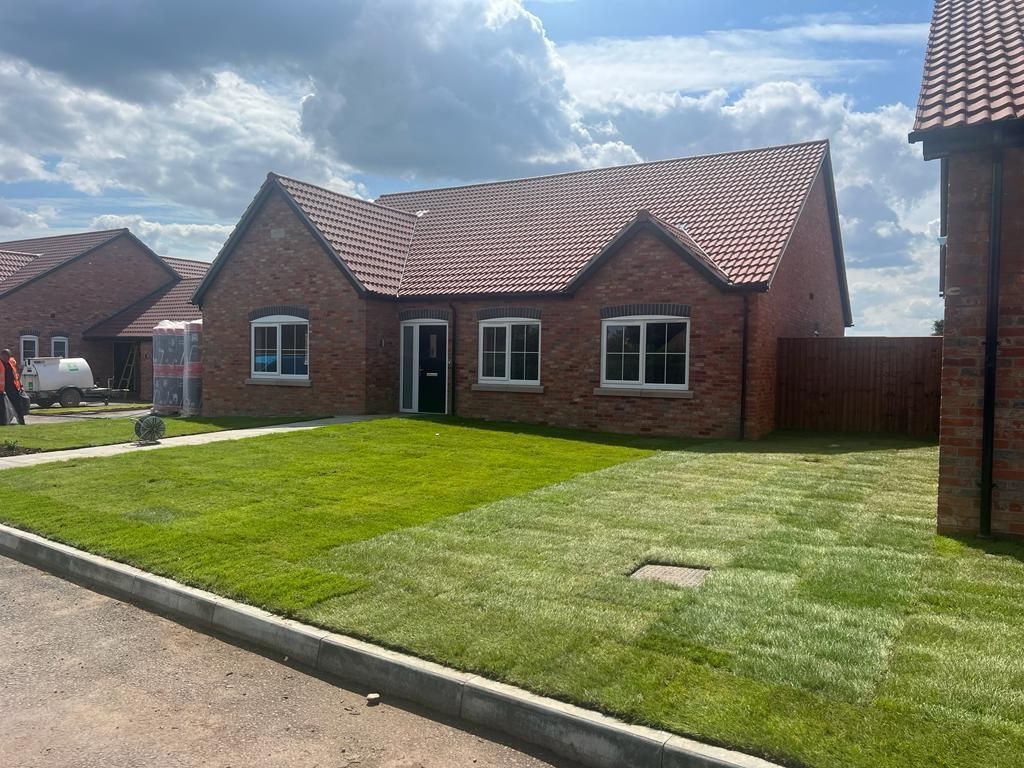 Red brick bungalow with a green lawn under a cloudy sky.
