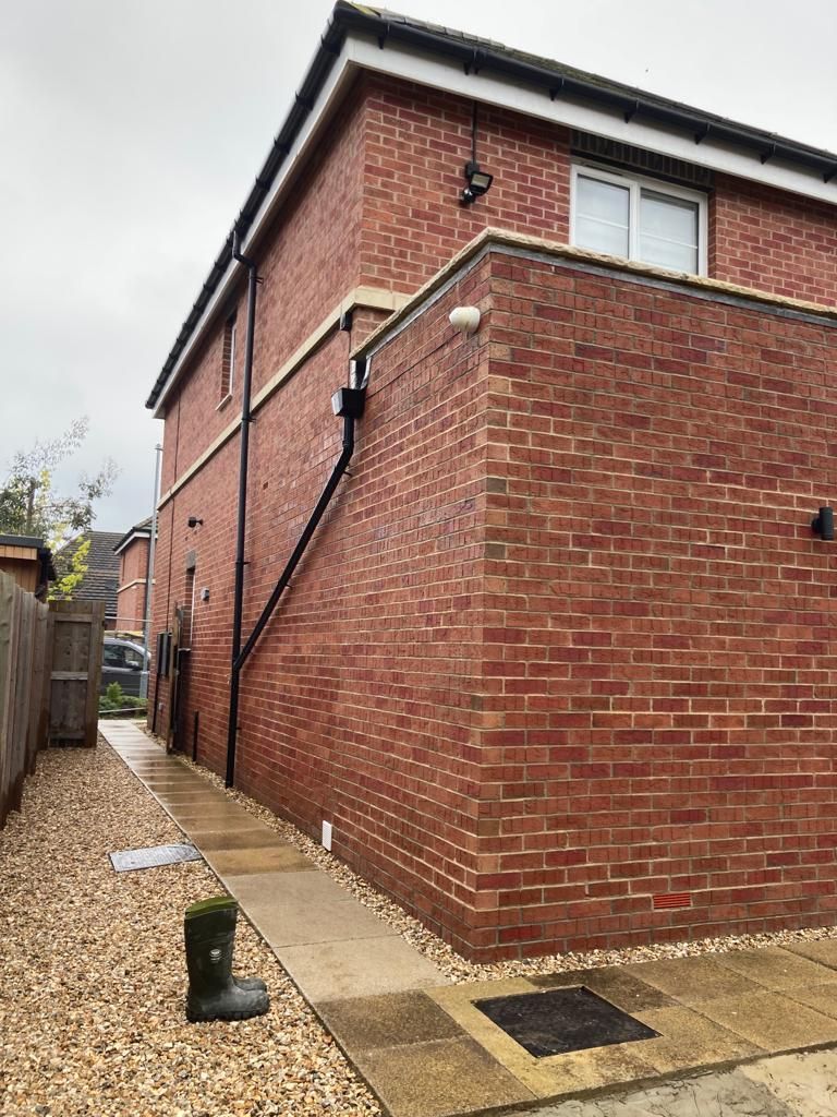 Brick building exterior with pathway; red brick, black gutter, gray gravel path, overcast day.