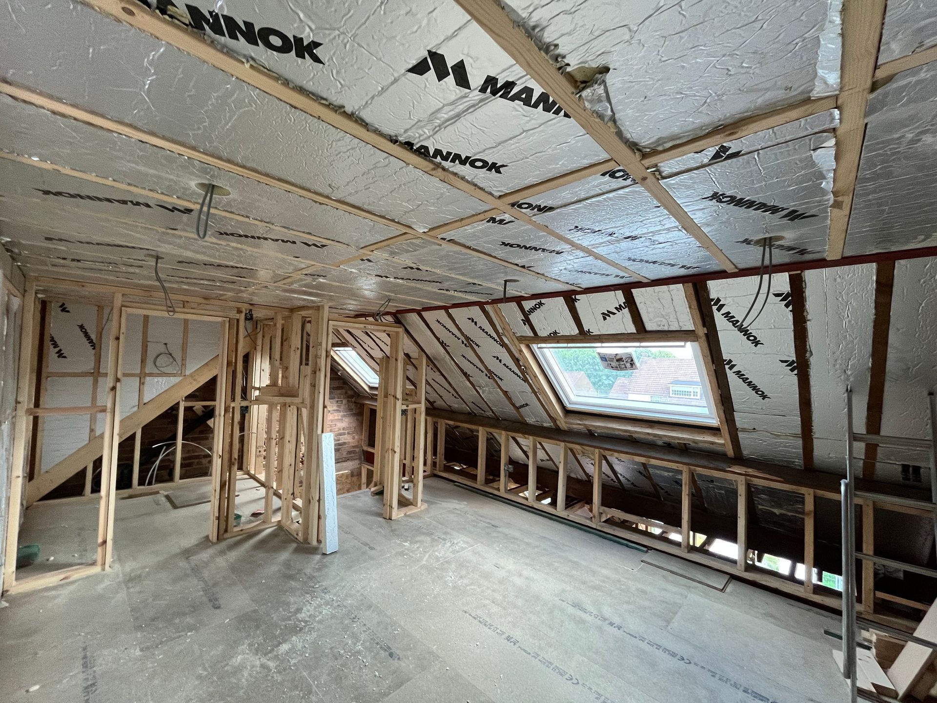 Interior of an attic under construction, with exposed wooden framing, insulation, and a skylight.