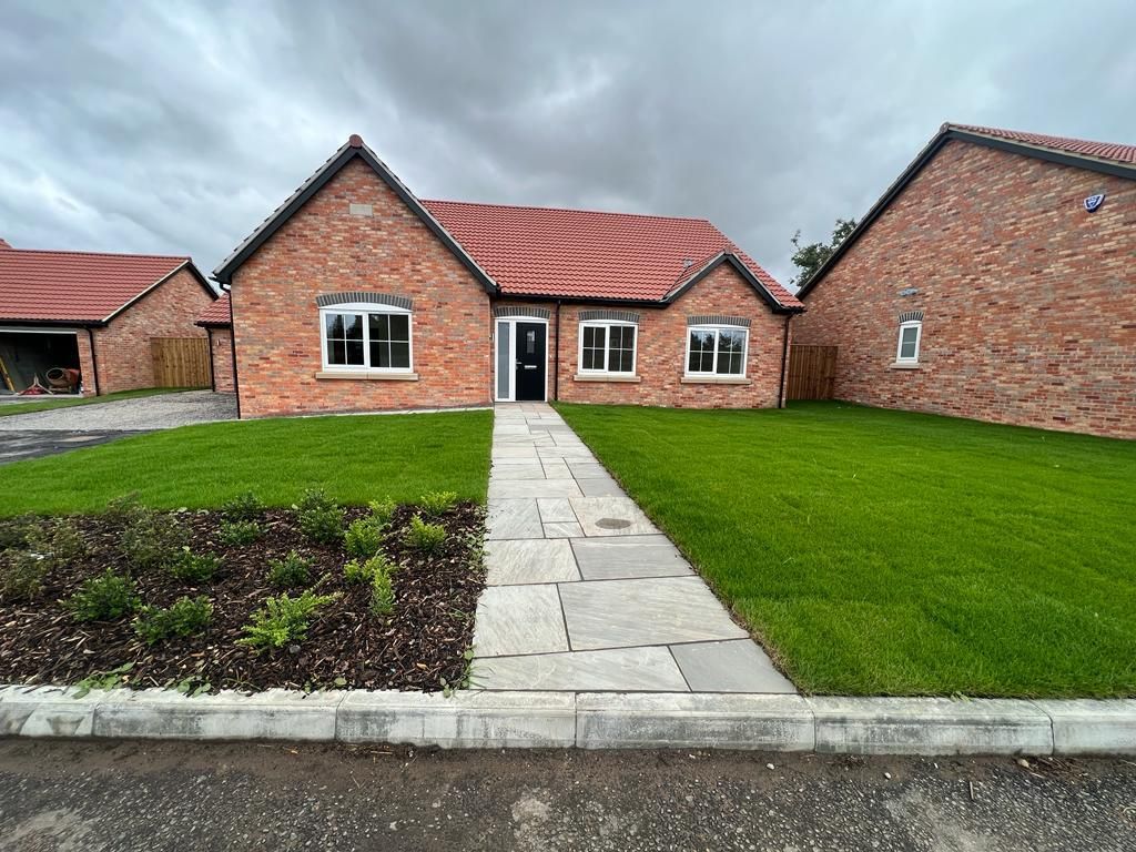 Brick bungalow with red roof, white-trimmed windows, a gray stone path, and green lawn.
