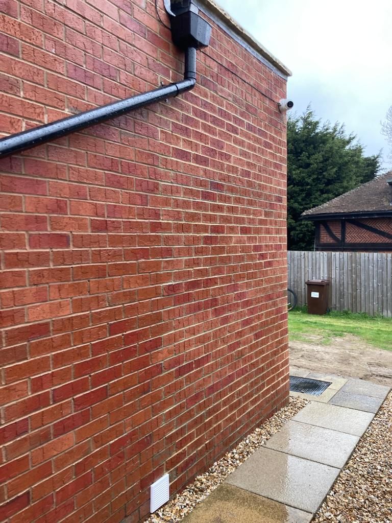 Red brick building exterior with black gutter, walkway, and a glimpse of yard.