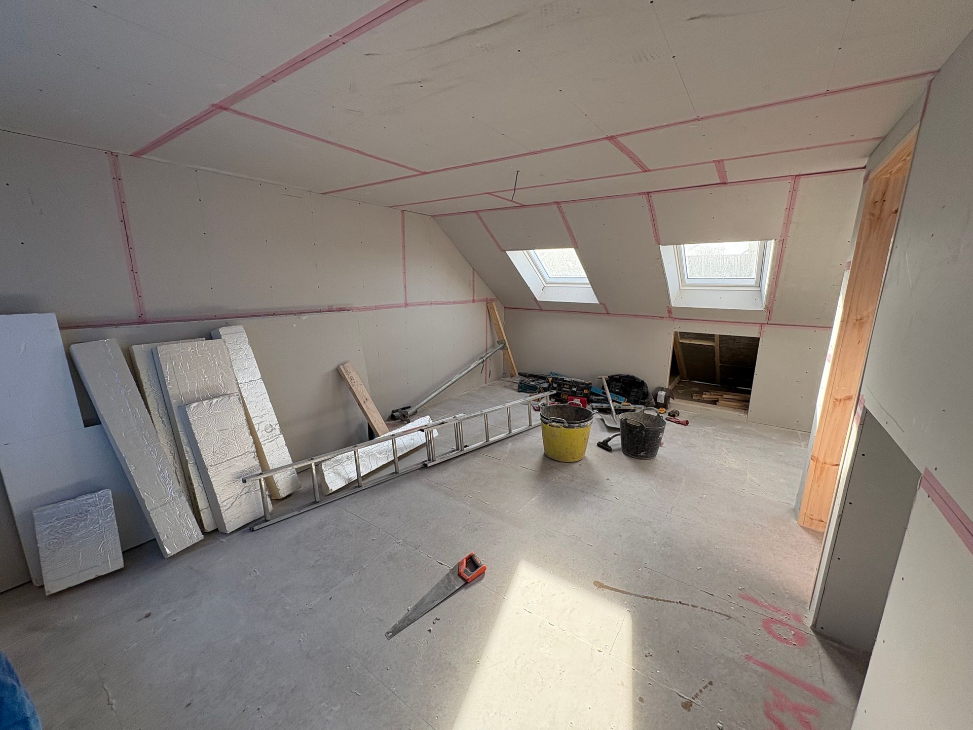 Room under construction; drywall installed on walls and ceiling, ladder and tools on floor.