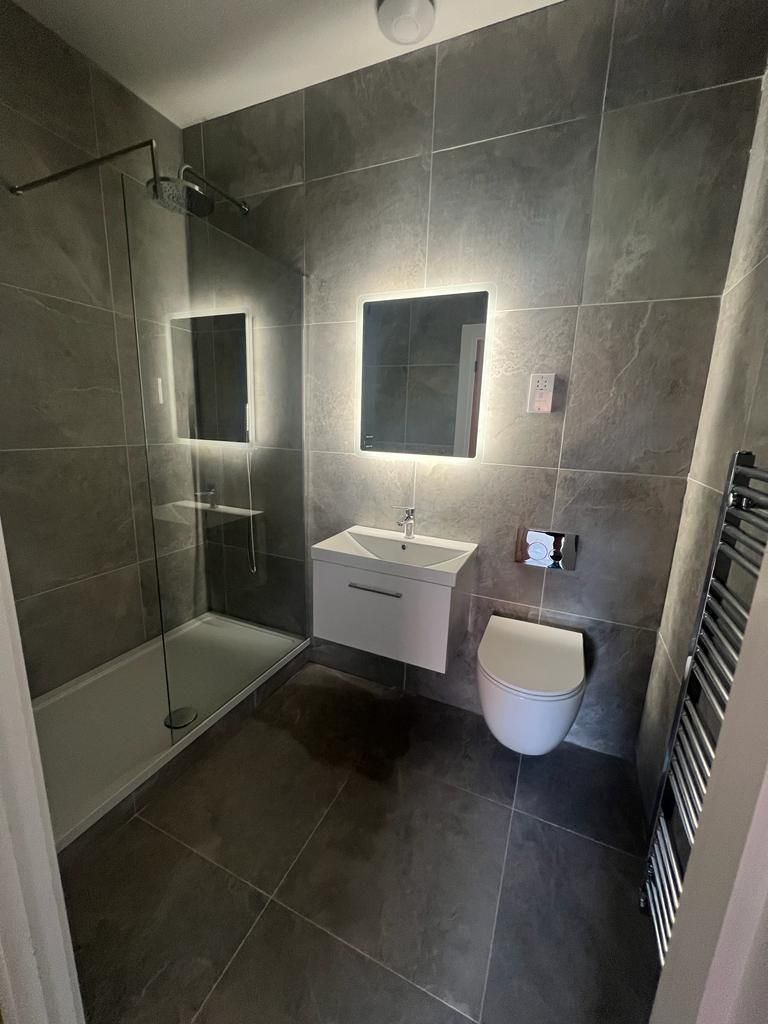 Modern gray tiled bathroom with a shower, floating sink, toilet, and heated towel rack.