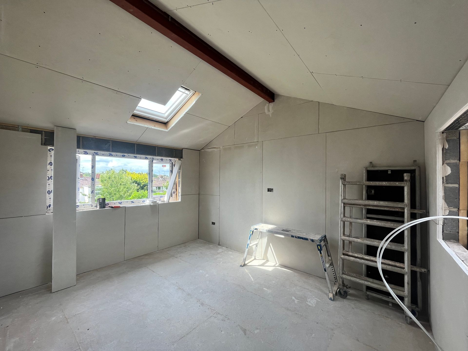 Interior of a room under construction, with drywall walls, a skylight, and scaffolding.