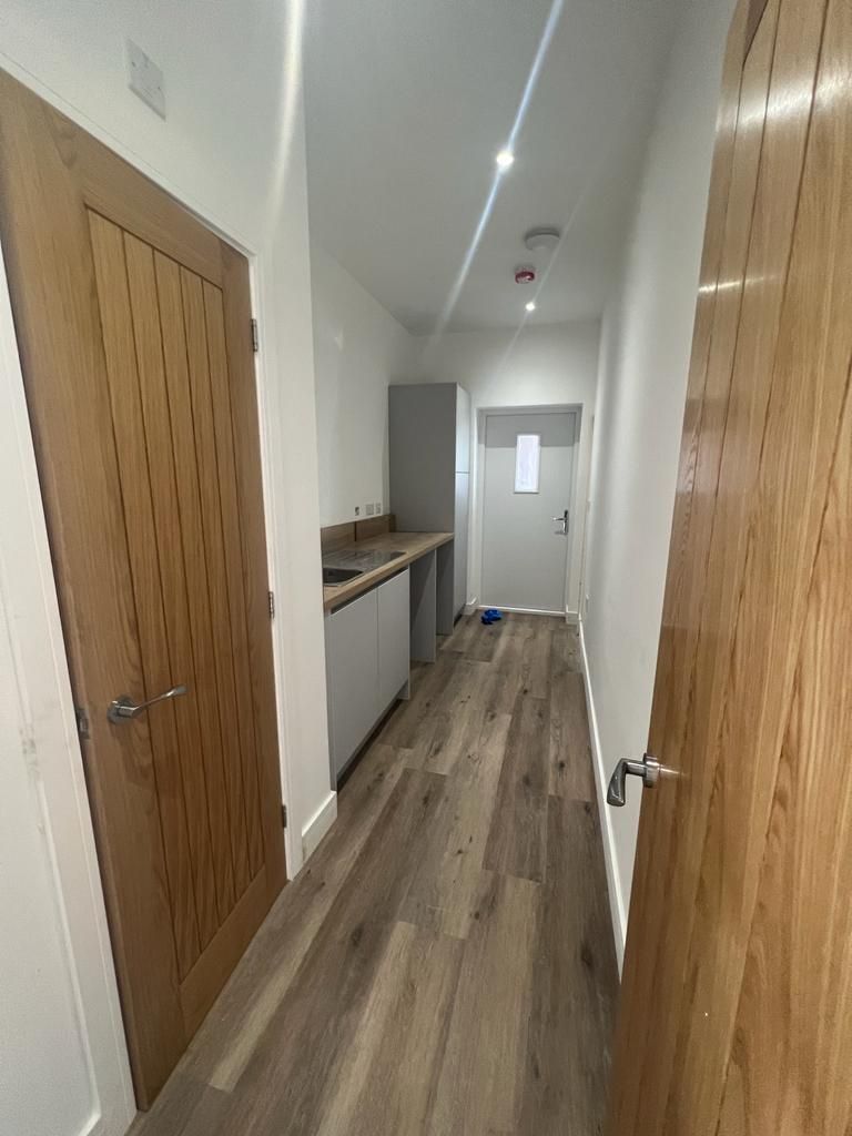 Narrow hallway with wooden doors and flooring, a small kitchenette, and a door at the end.