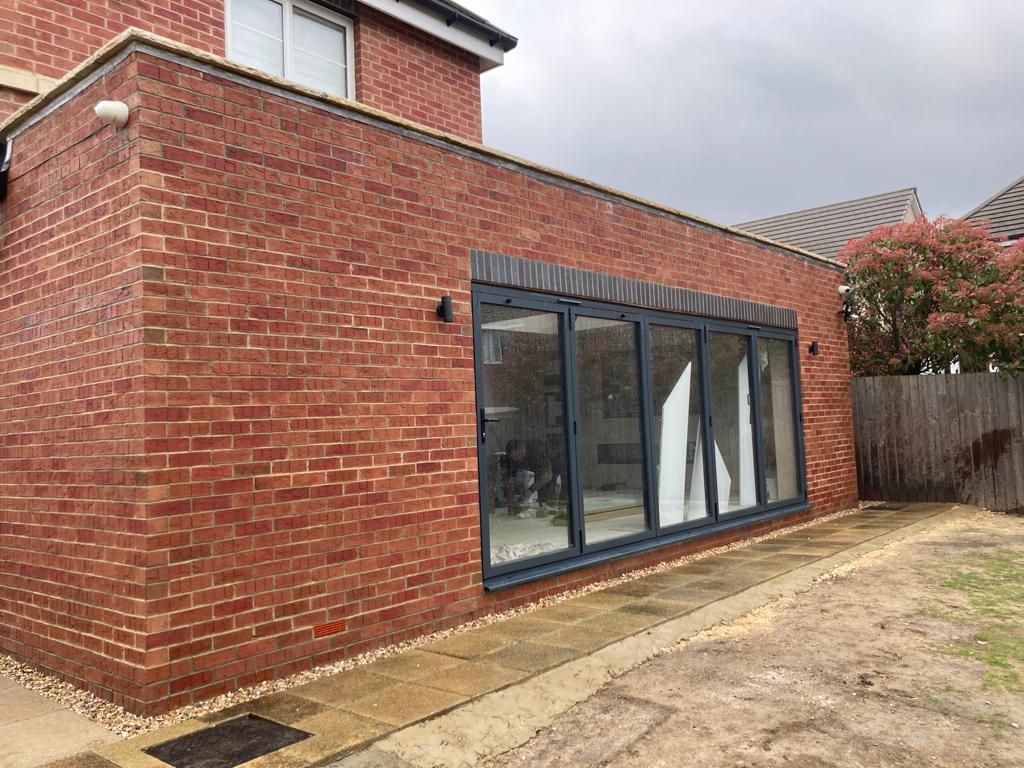 Red brick house extension with gray framed folding glass doors.