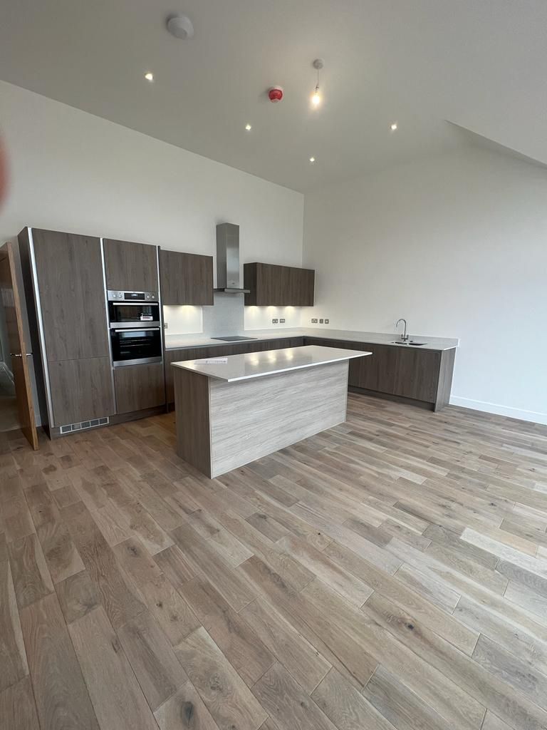Modern kitchen with wooden cabinets, island, and flooring. Gray countertops, stainless steel appliances, and white walls.
