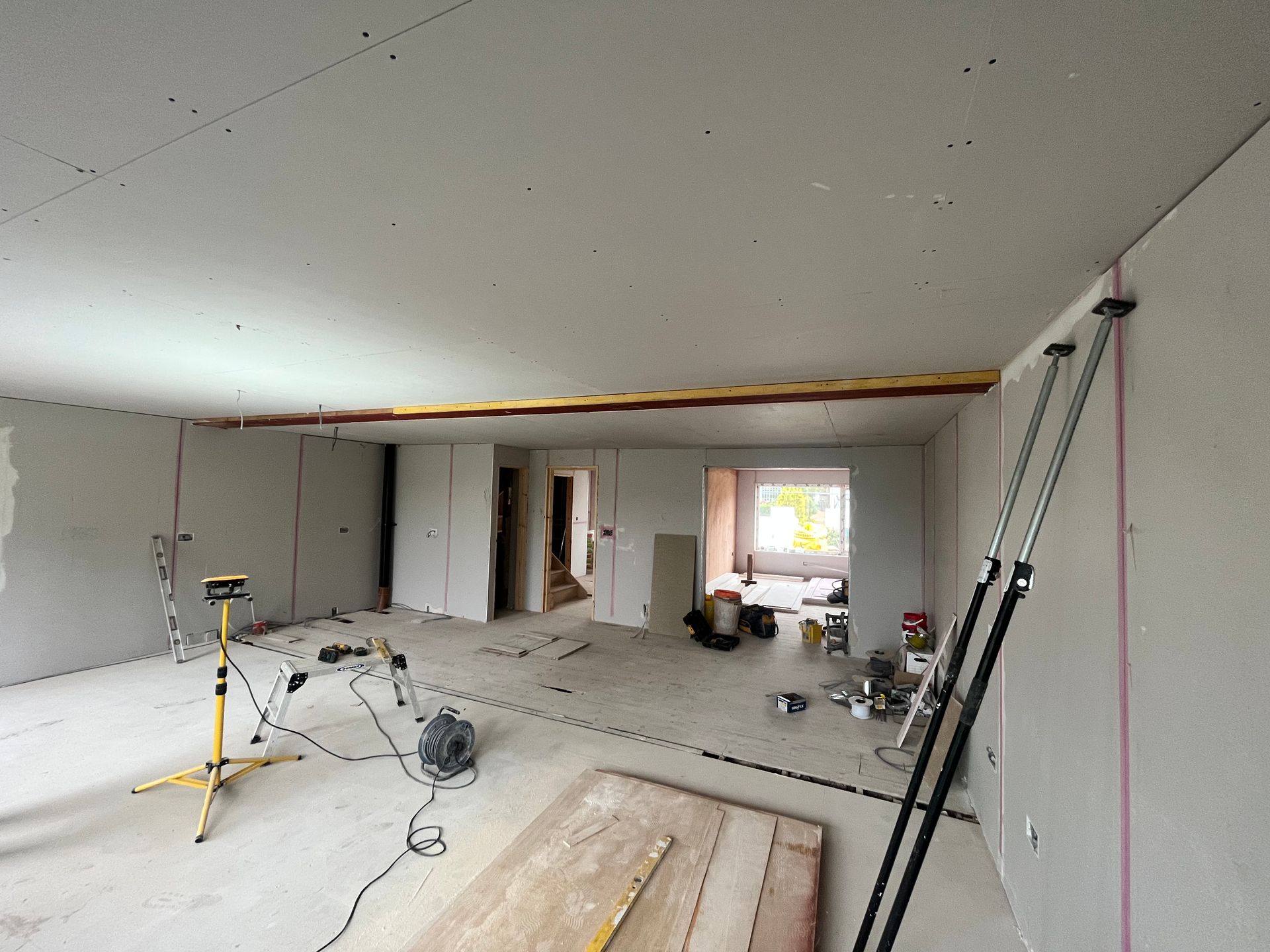 Interior view of a room under construction. Drywall installed, red laser lines, tools scattered on the floor
