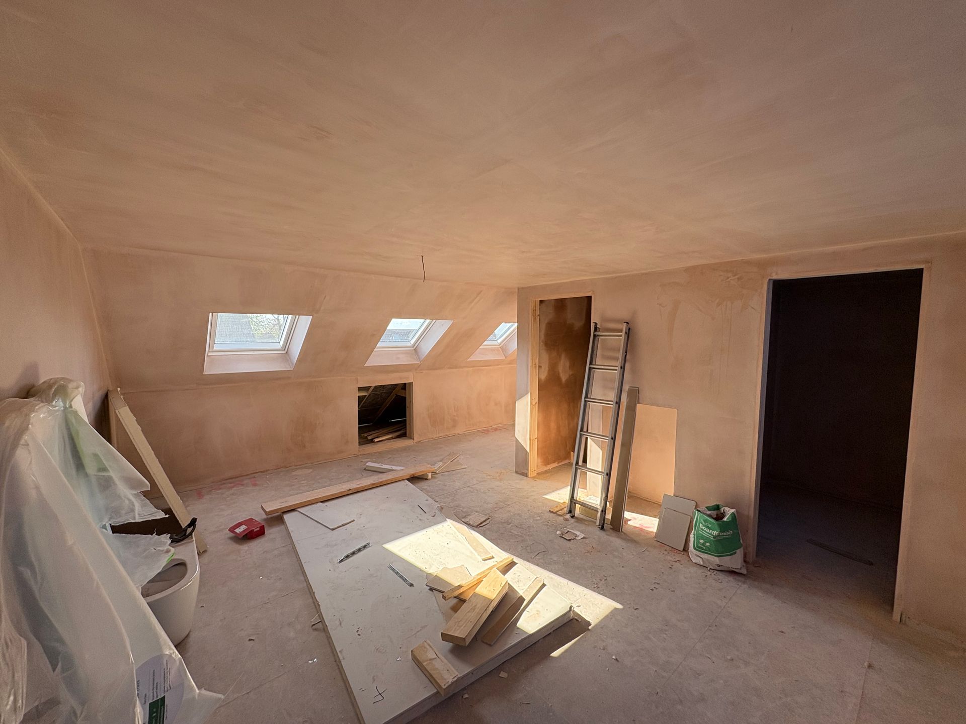 Interior of a room under construction with slanted ceiling, skylights, and door.