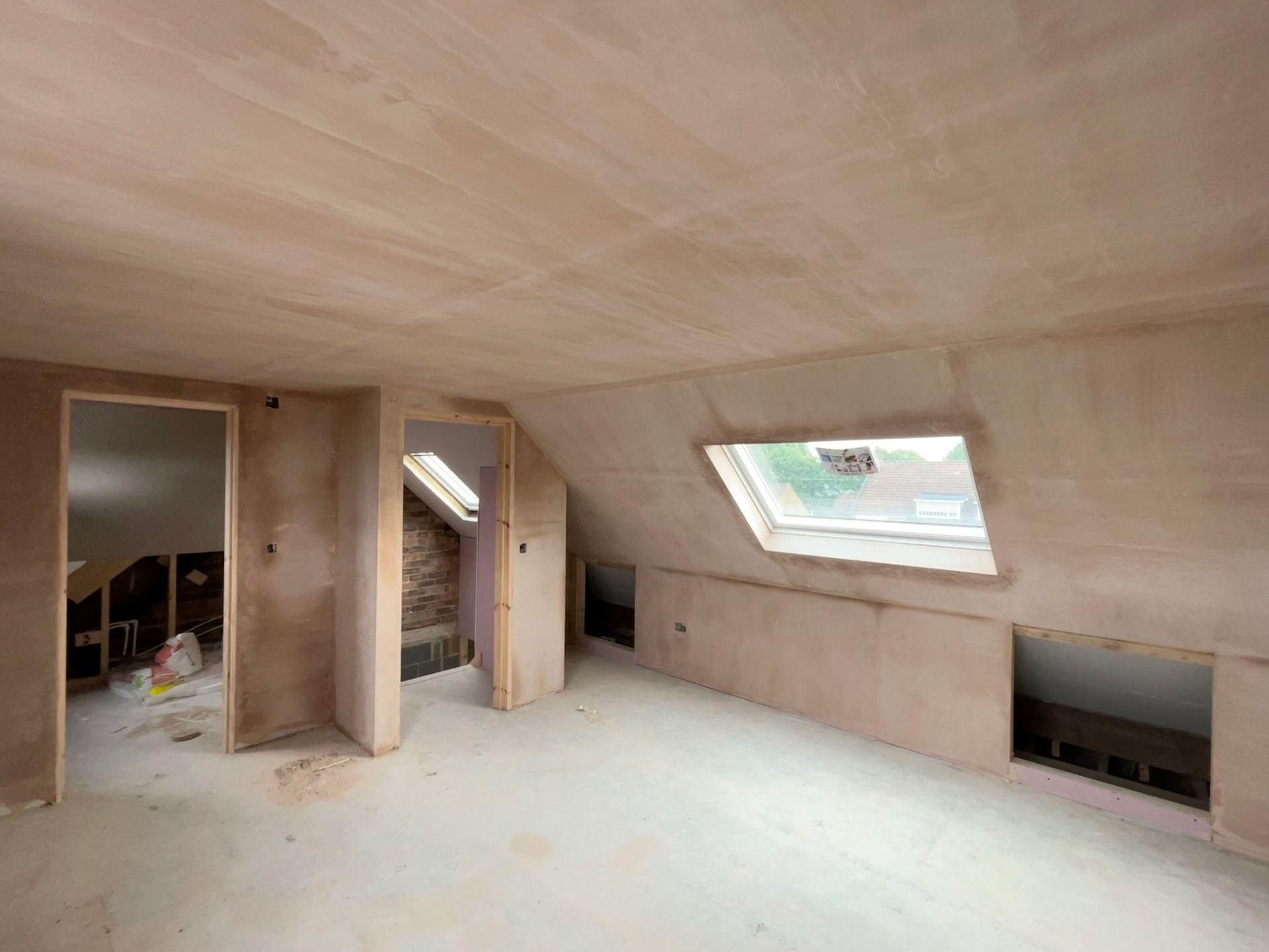 Newly plastered attic room with skylight, doorways, and knee walls, ready for finishing.