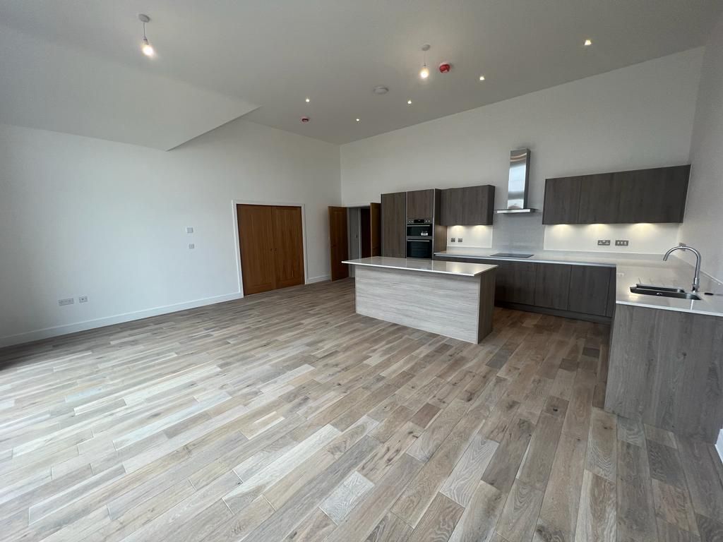 Open-plan kitchen with wooden floors, gray cabinets, island, and white walls.