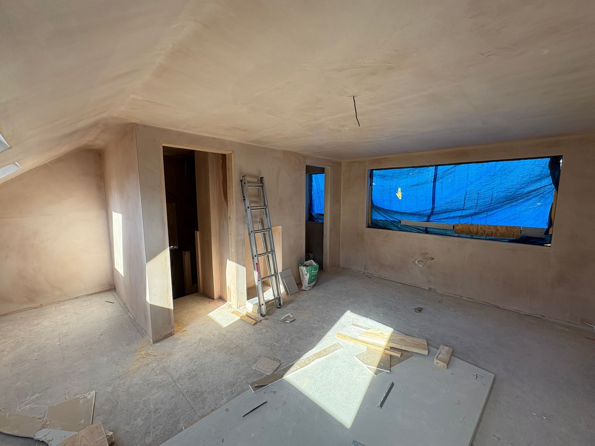 Room under construction with freshly plastered walls and covered windows.