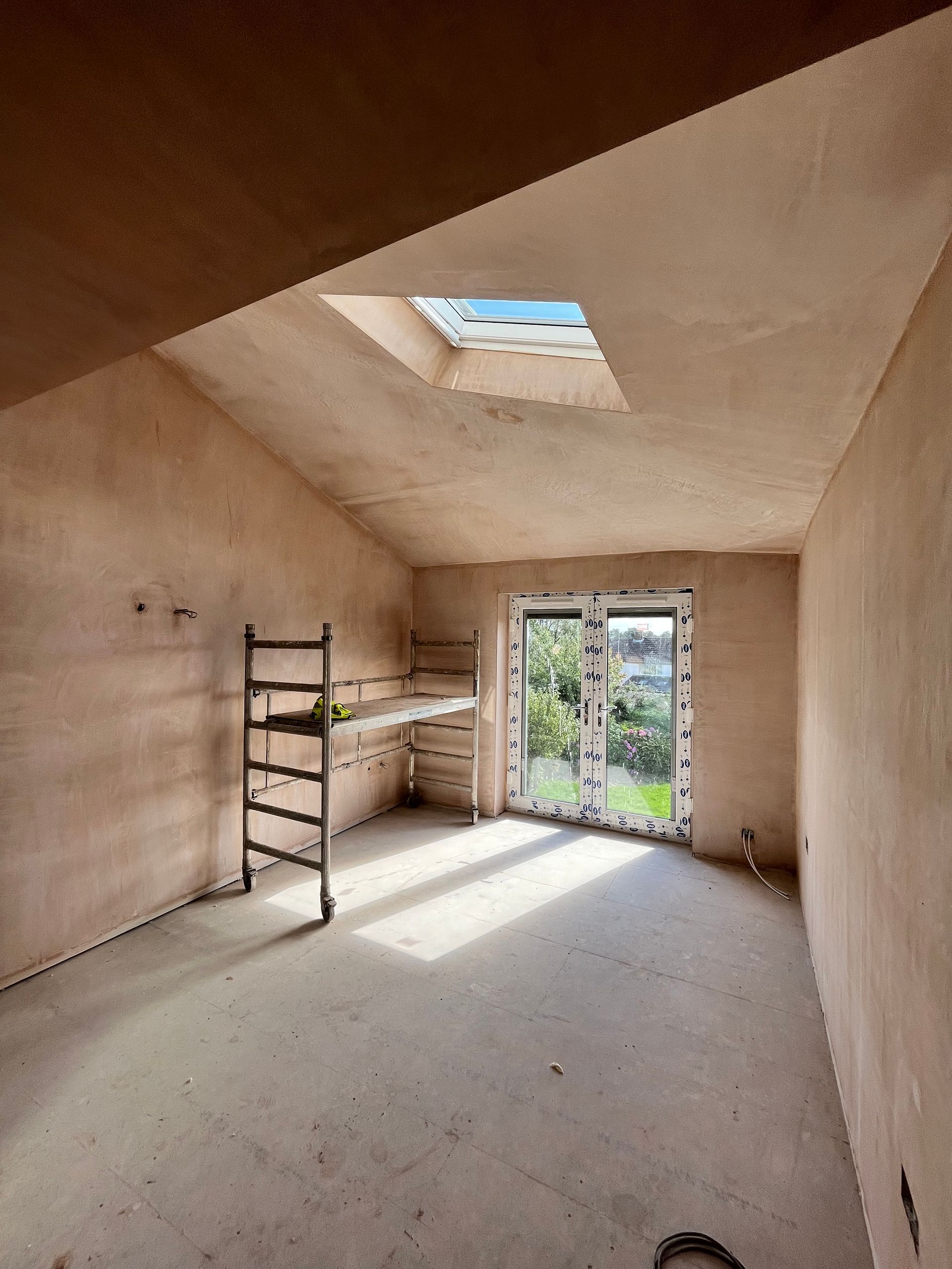 Newly plastered room with skylight, door to a garden, and a metal scaffolding.