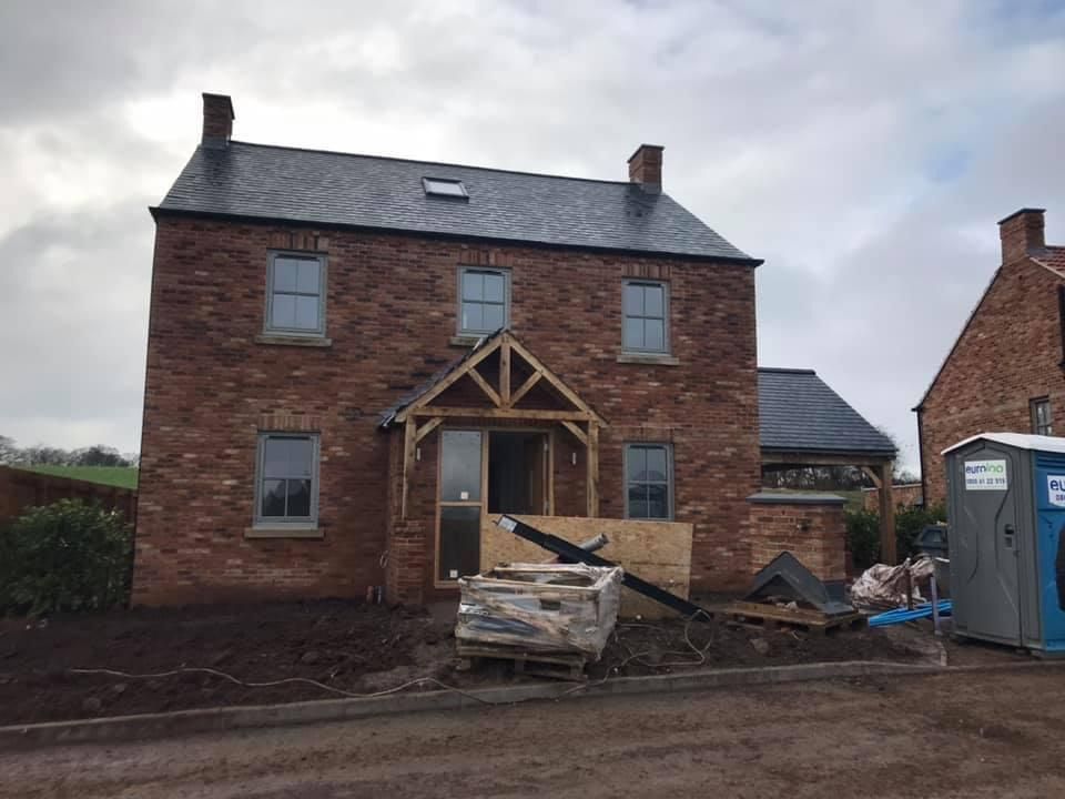 Red brick house under construction; gray roof, windows, and doorway with wooden frame.