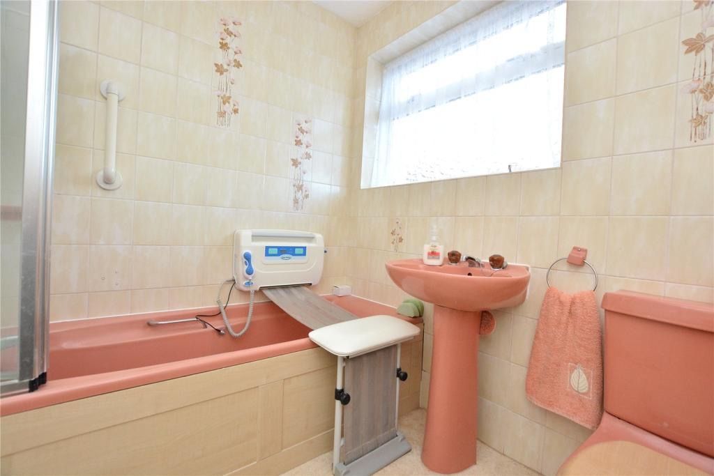 Bathroom with a pink bathtub, sink, and toilet; a bath lift is installed near the tub.