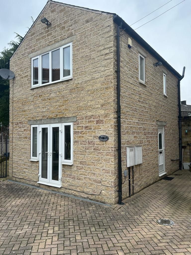 Two-story brick building with white doors/windows, on a cobblestone driveway.