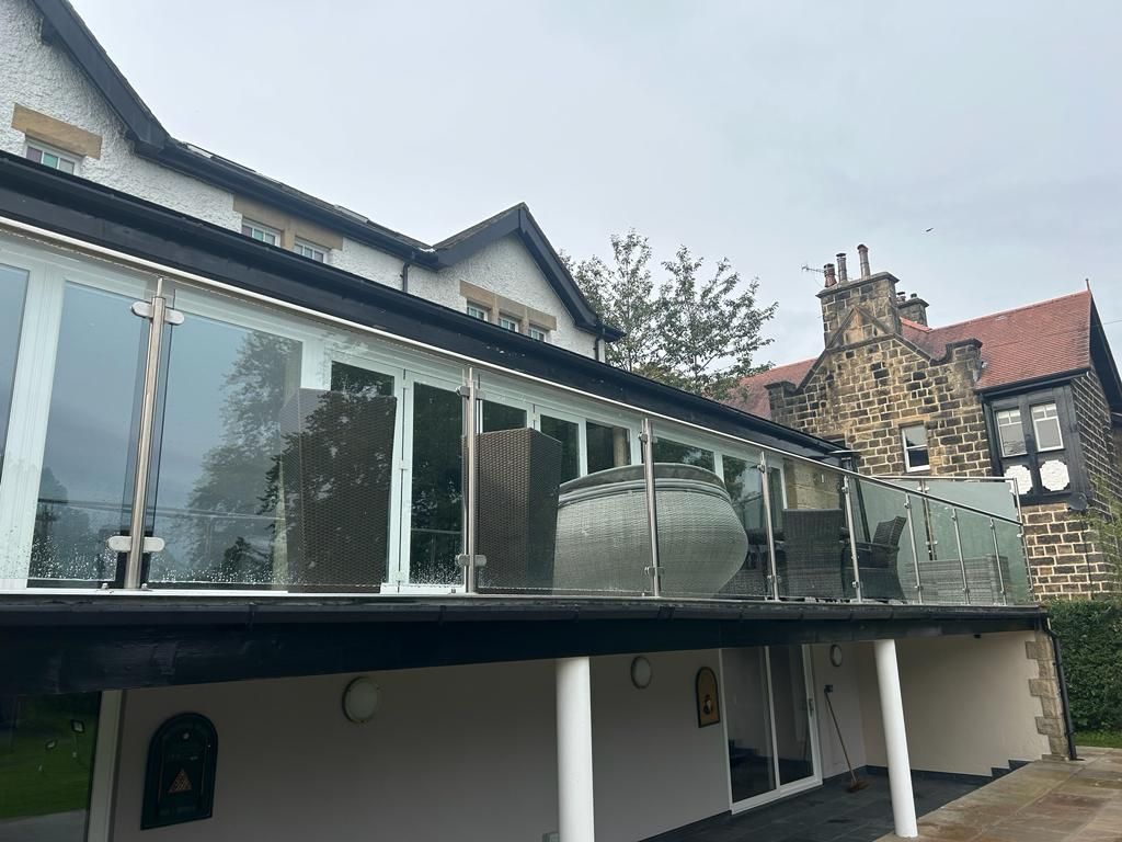 Balcony with glass railing and hot tub, attached to a white house, overlooking a green lawn.