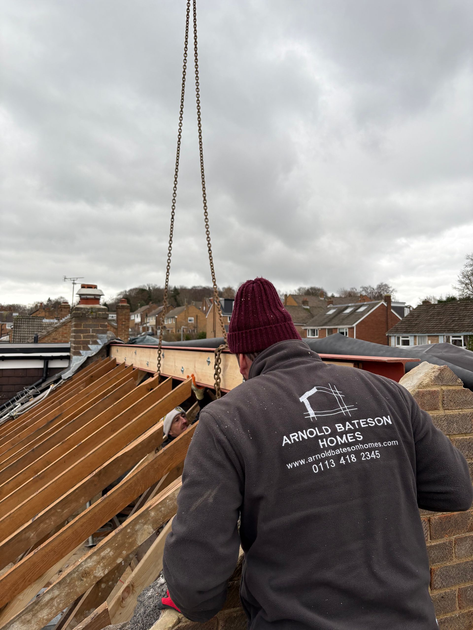 Construction workers lifting a wooden beam onto a roof with a crane on a cloudy day.