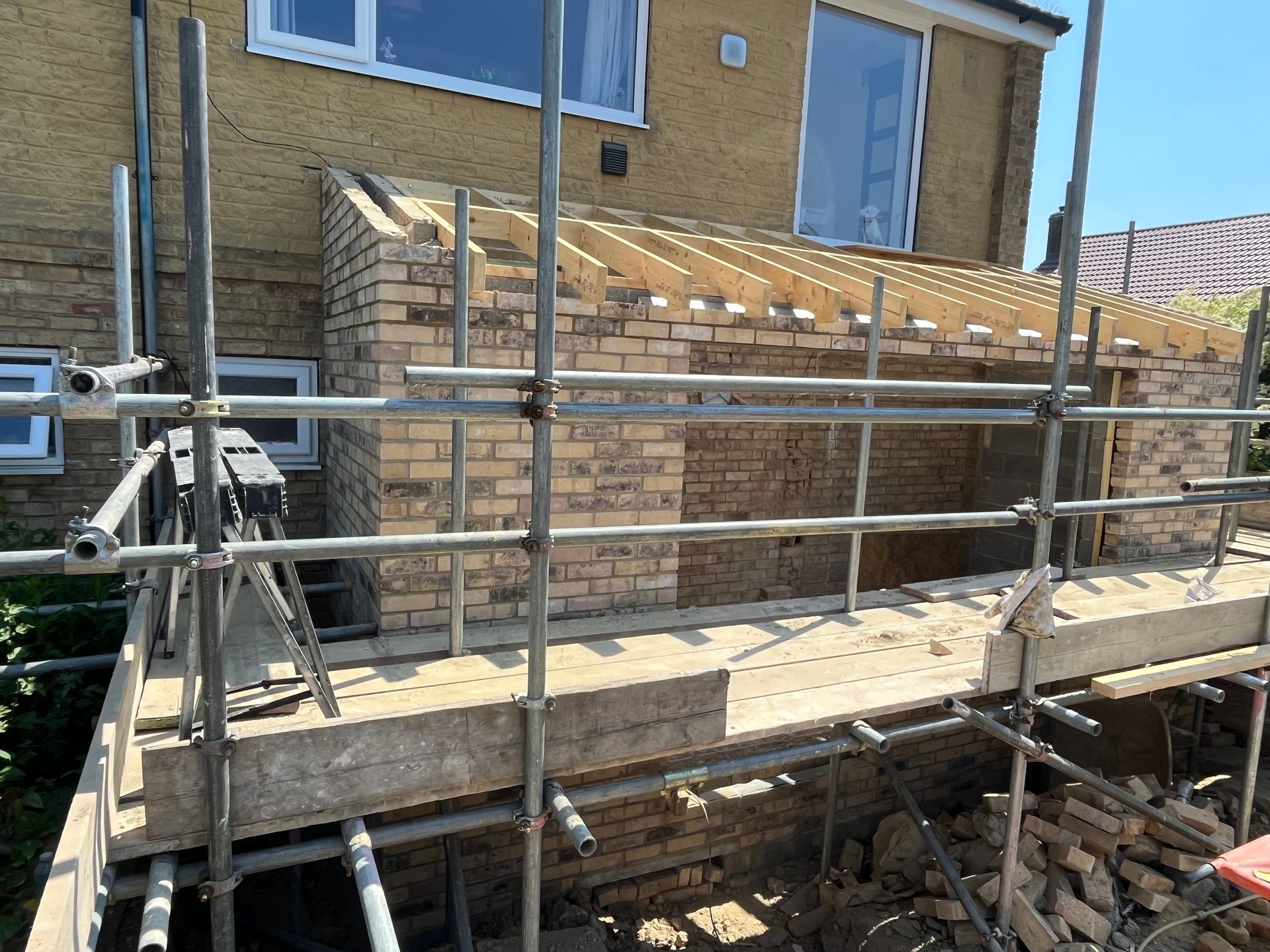 Construction of a brick home extension with scaffolding. Yellow brick, unfinished roof, bright sky.