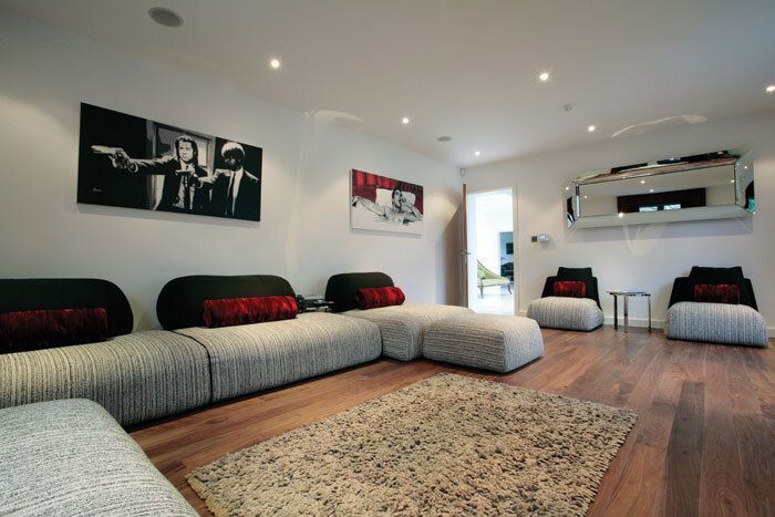 Modern living room with a long gray sectional sofa, red pillows, and art on white walls.