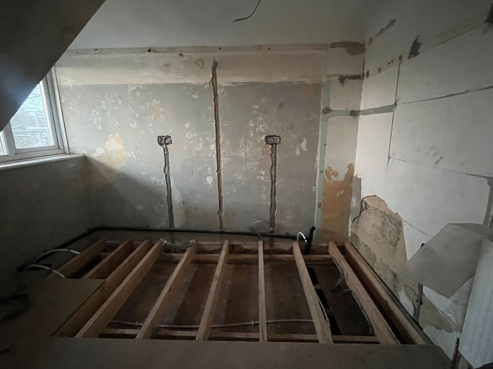 Interior view of a room under construction, with wooden floor supports and unfinished walls.