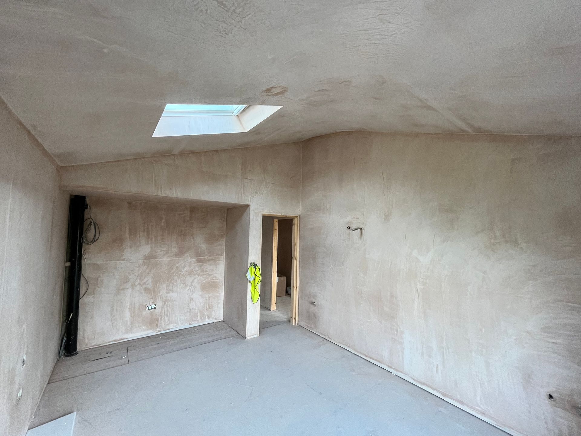 Room interior under construction; unfinished walls, skylight in ceiling, door visible.