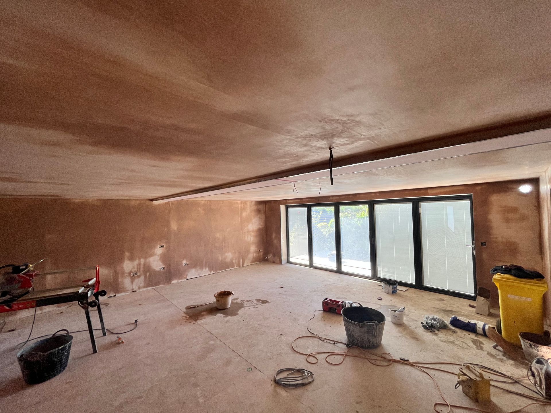 Interior construction with exposed plaster walls, a large window, and tools.
