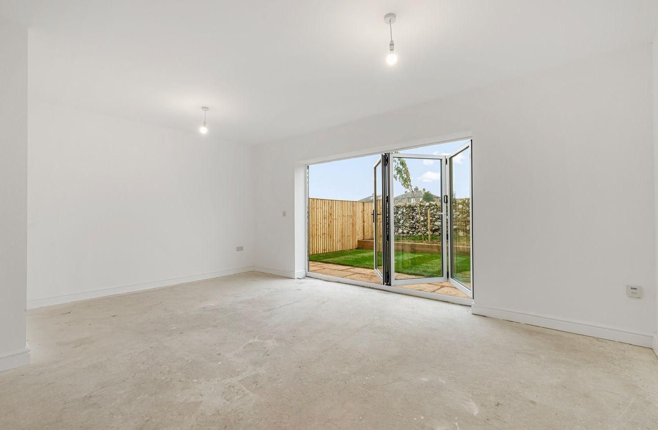 Empty room with open folding glass doors to a backyard. White walls, beige carpet, and natural light.