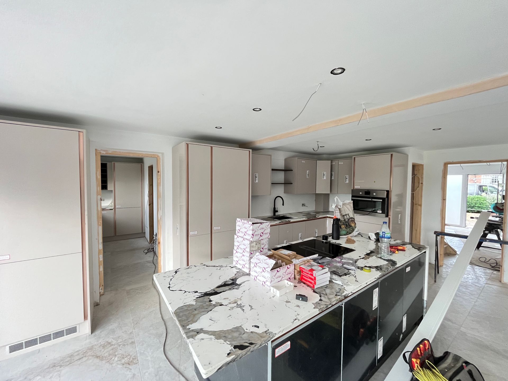 Kitchen under construction; light cabinets, dark island with white countertop, tools, and unfinished trim.