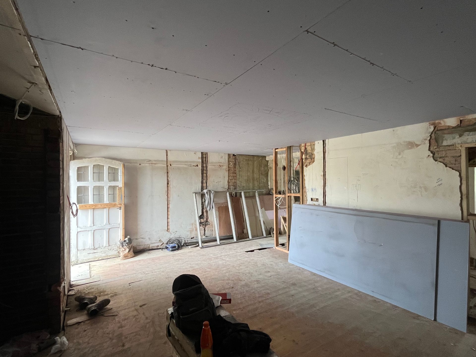 Room under renovation, drywall installed on the ceiling, exposed framing and walls, natural light.