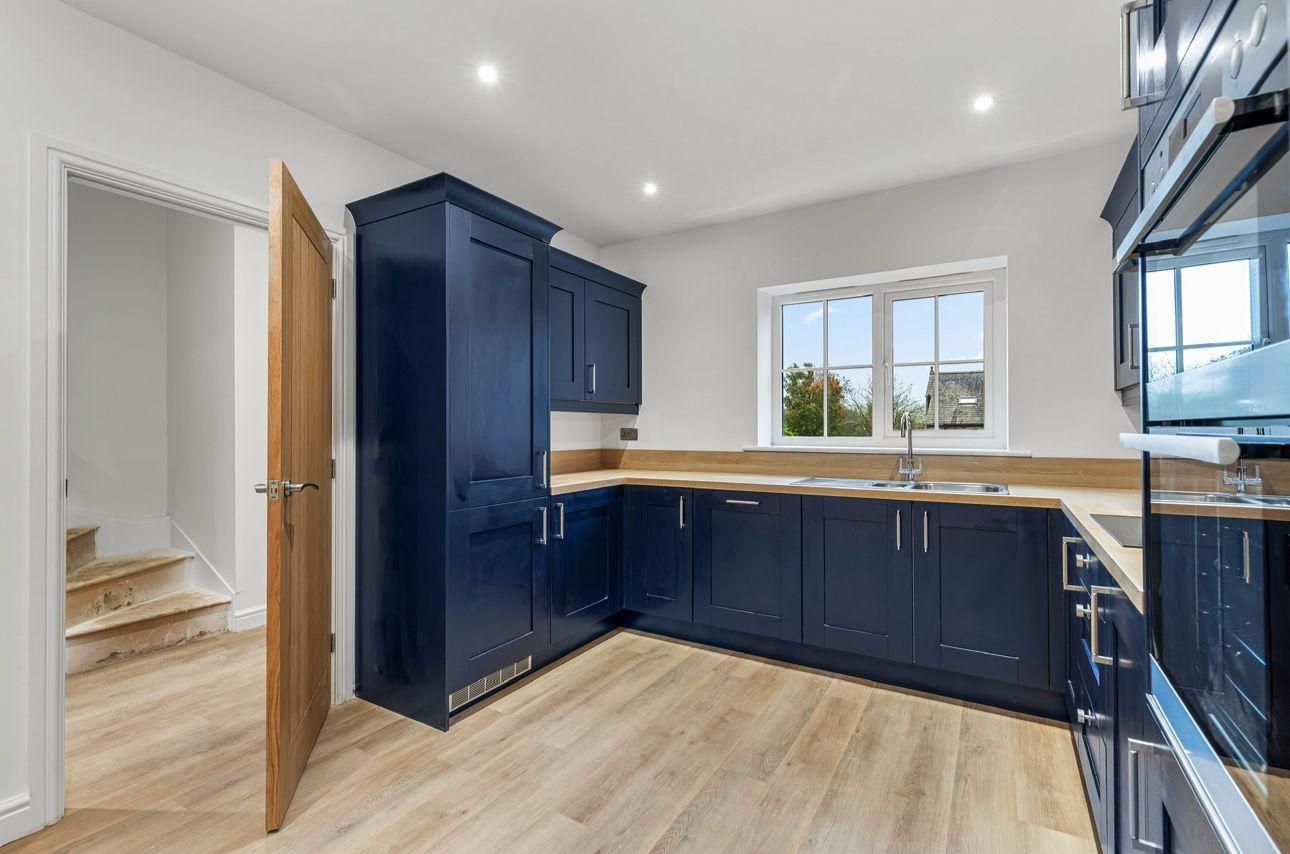 Blue kitchen cabinets with light wood countertops and flooring, near a window and open doorway.