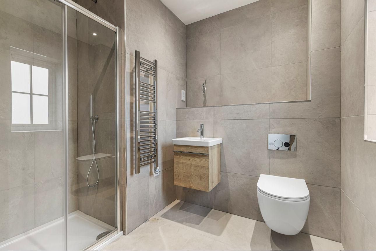 Modern bathroom with a shower, sink, and toilet; light gray walls and wood-tone cabinet.