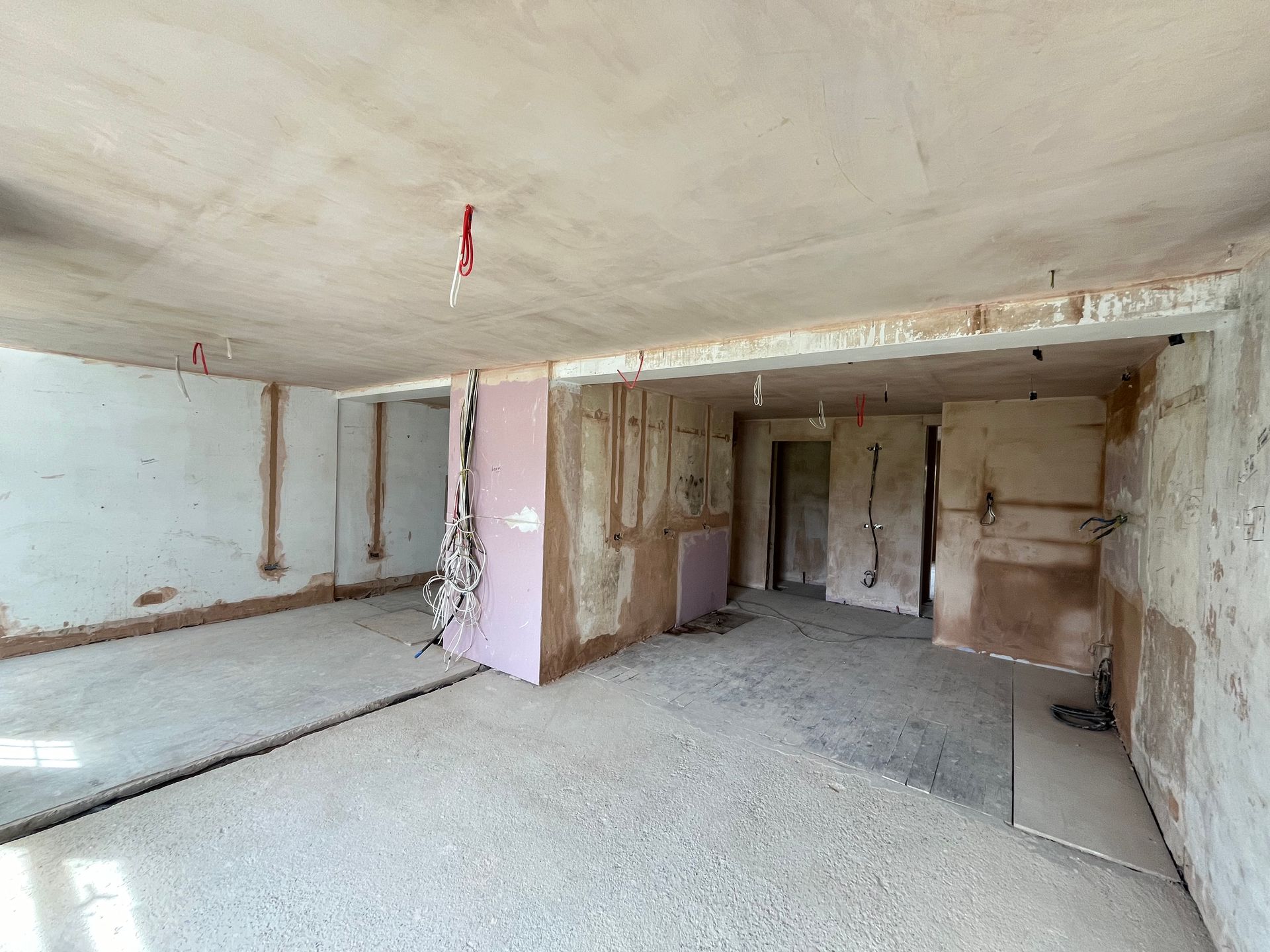 Interior room under renovation, exposed wiring, pink insulation, concrete floor, plaster walls.