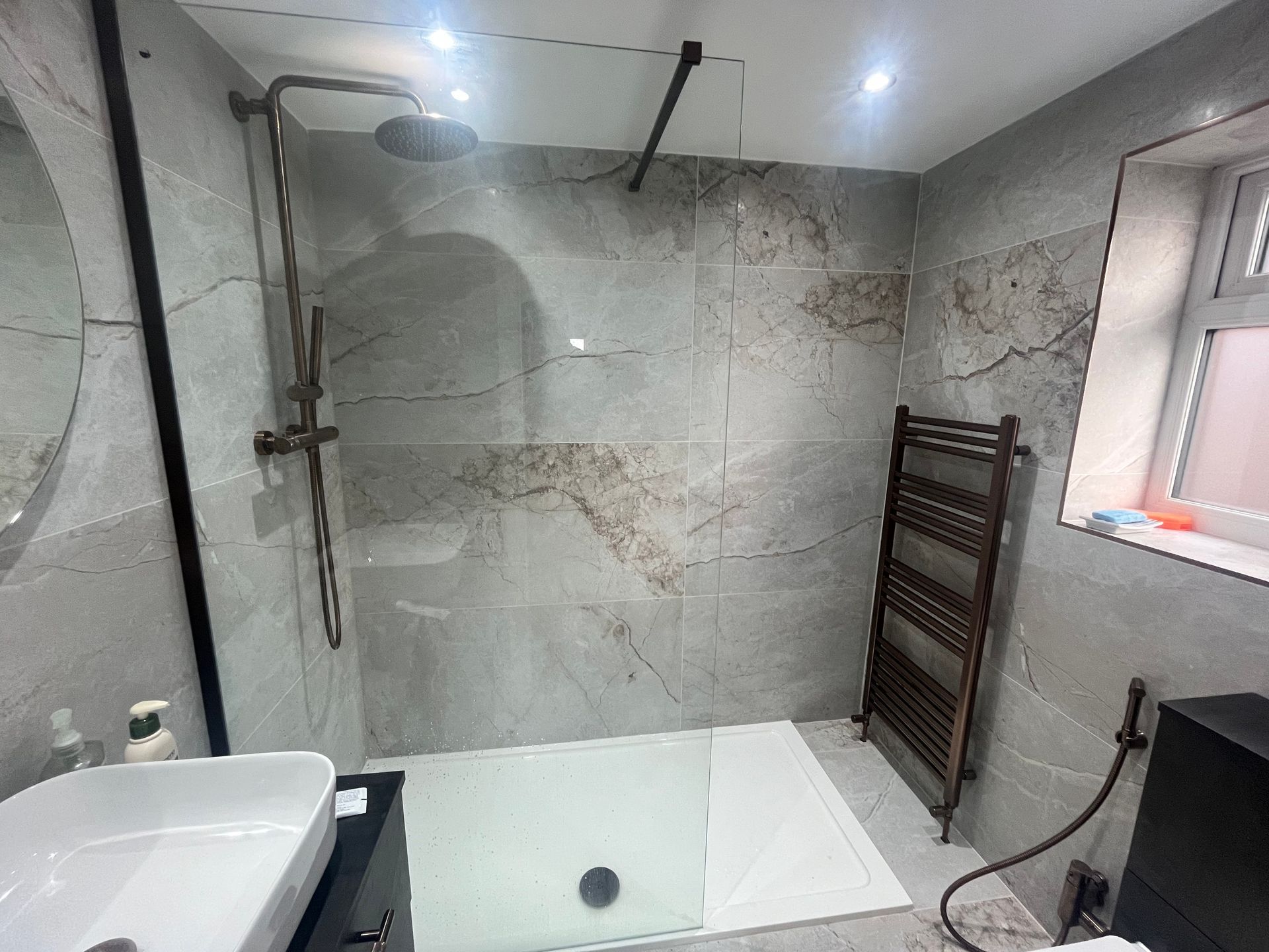 Modern bathroom with a gray tiled shower, black fixtures, and heated towel rack.