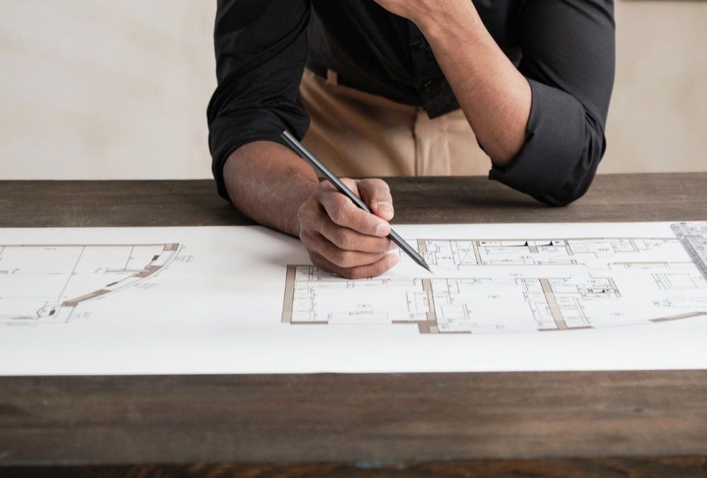 Person leaning on a table with a pencil, working on architectural plans.