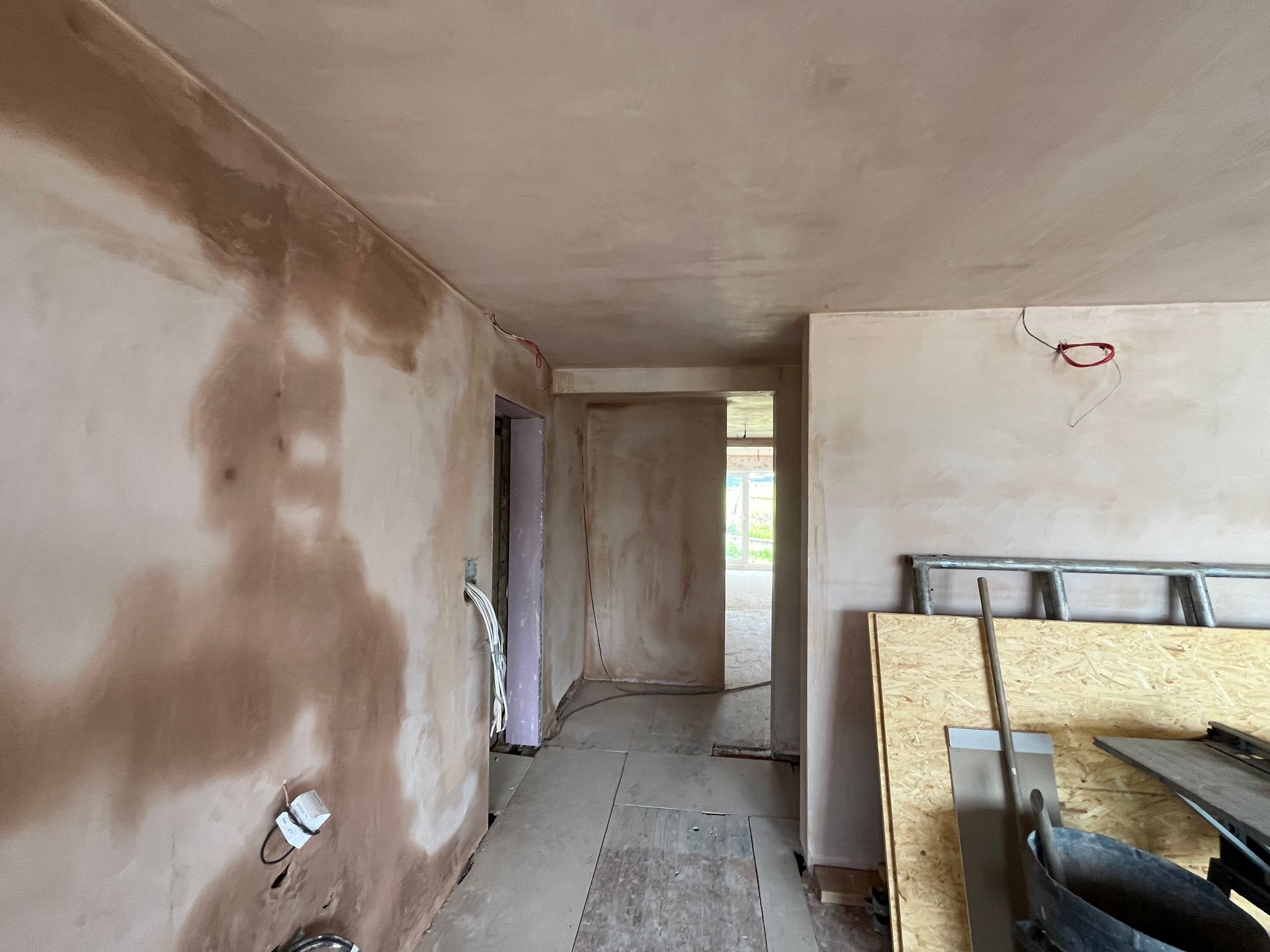 Interior hallway under construction with unfinished plaster walls and ceiling.