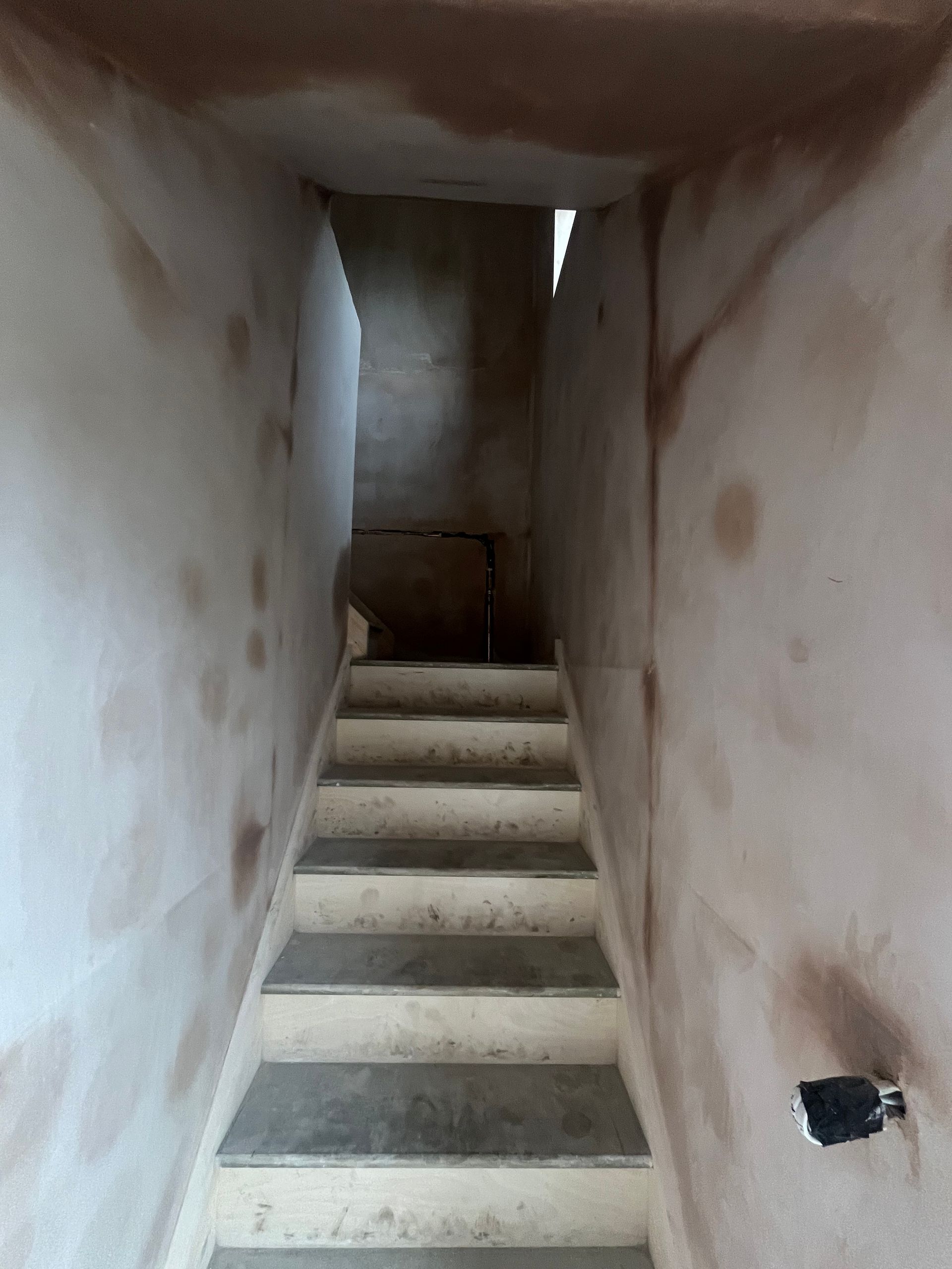 Staircase with concrete steps, unfinished walls with brown marks.  The opening at the top is visible.