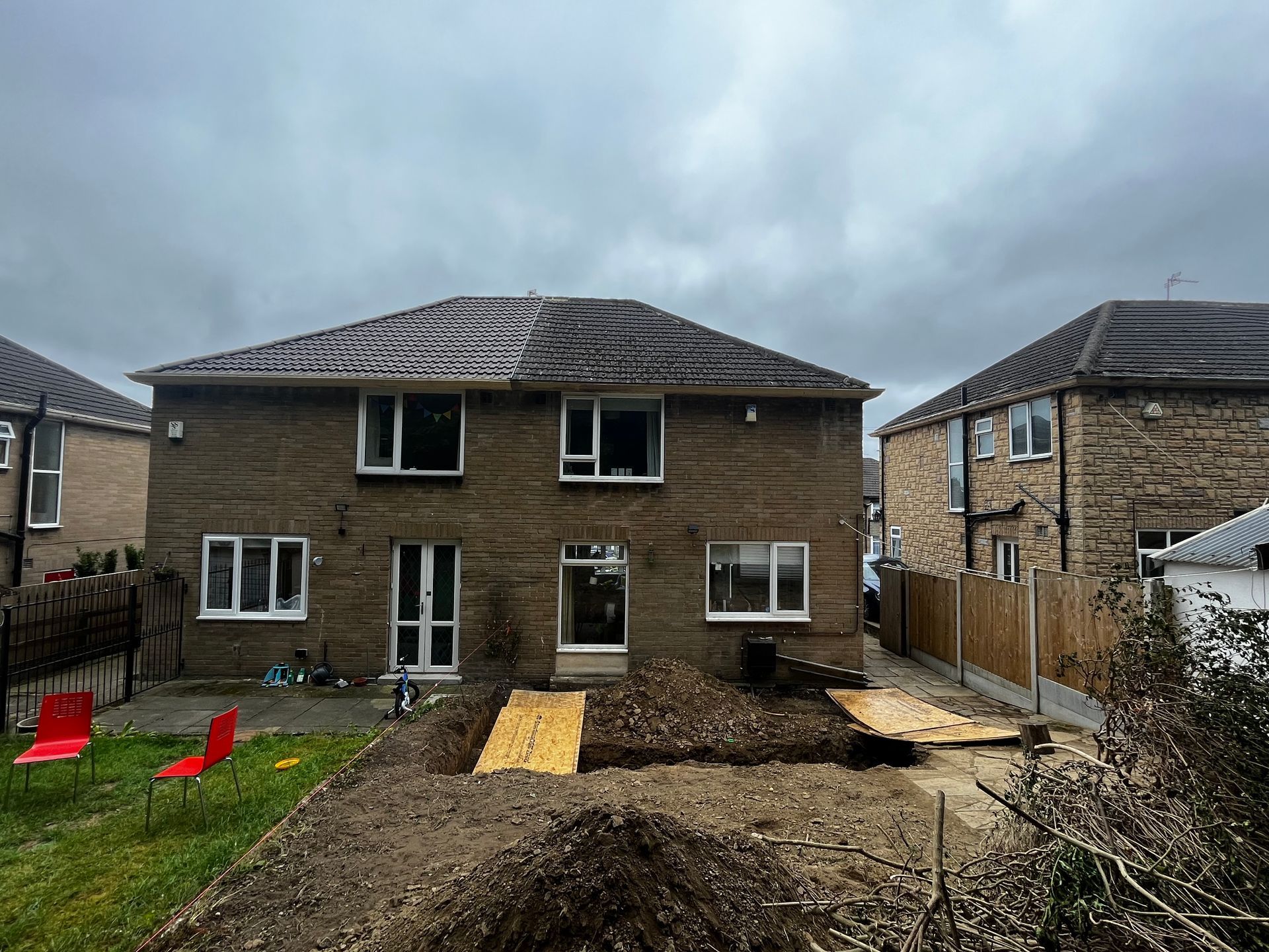 Backyard of a two-story brick house with construction; overcast sky.